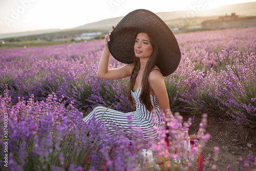 Pretty girl is wearing big hat sitting in lavender field, France.