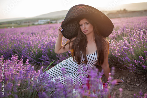 Pretty girl is wearing big hat sitting in lavender field, France.