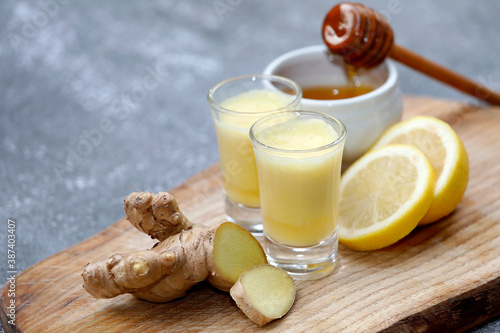 Ginger shot or drink with healthy ingredients like ginger root, honey and lemon on wooden background.