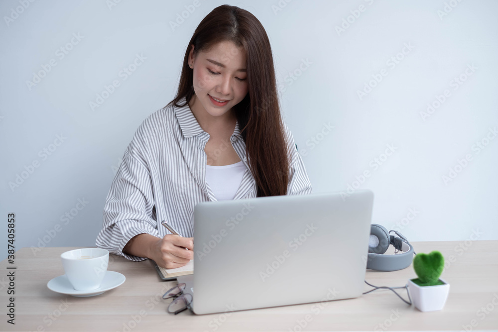 Young Asian women wear headphones using their laptop inside the office, working for online lessons or listening to webinars. Young Asian women wear headphones using their laptop inside the office, working for online lessons or listening to webinars.