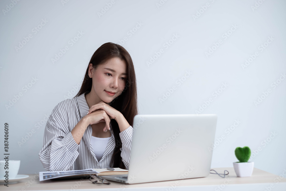 Portrait of a happy face Asian woman sitting at home working on a laptop while sitting on a desk. To come up with business design ideas Portrait of a happy face Asian woman sitting at home working on a laptop while sitting on a desk. To come up with business design ideas