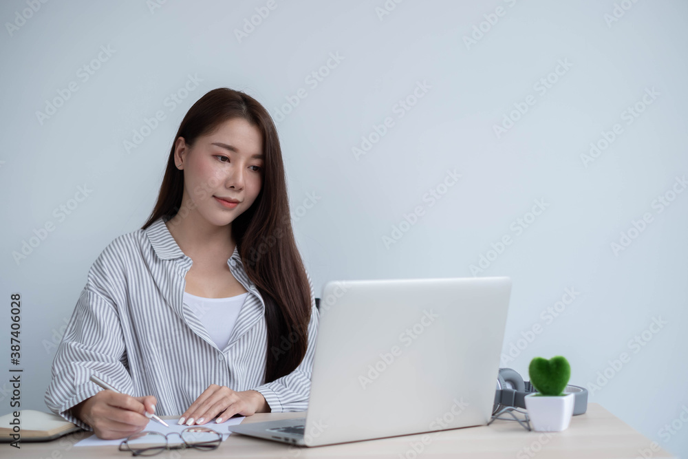 Portrait of a happy face Asian woman sitting at home working on a laptop while sitting on a desk. To come up with business design ideas Portrait of a happy face Asian woman sitting at home working on a laptop while sitting on a desk. To come up with business design ideas