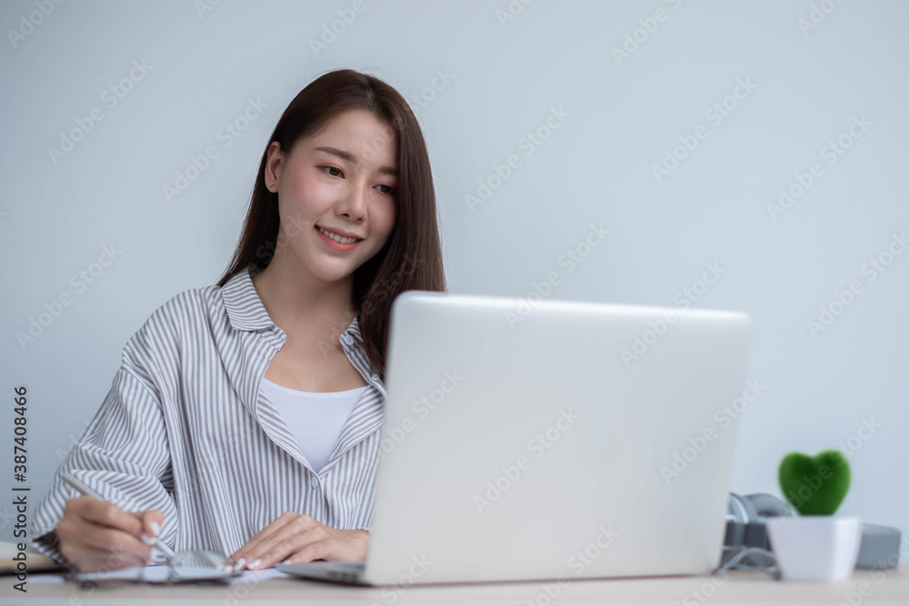 Young Asian women spend their free time using their laptop to educate themselves online and take notes., work from home concept. Young Asian women spend their free time using their laptop to educate themselves online and take notes., work from home concept.