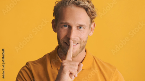 Attractive smiling bearded man showing keep secret to friend isolated on yellow background