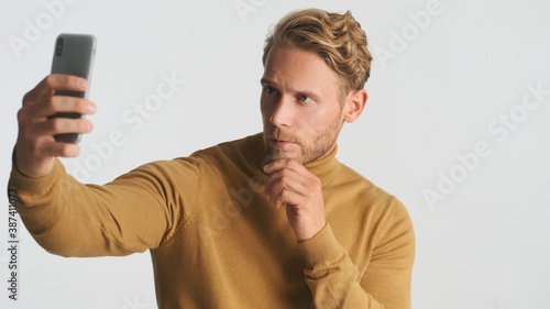 Handsome stylish bearded man taking selfie on smartphone over white background. Male model posing in studio