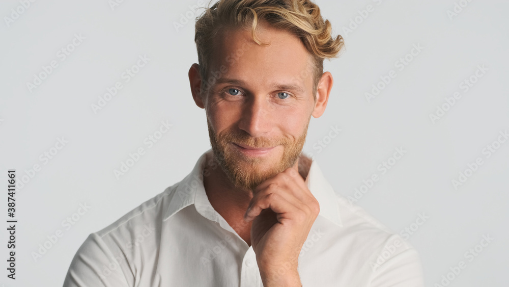 Obraz premium Attractive blond bearded man confidently looking in camera and smiling over white background