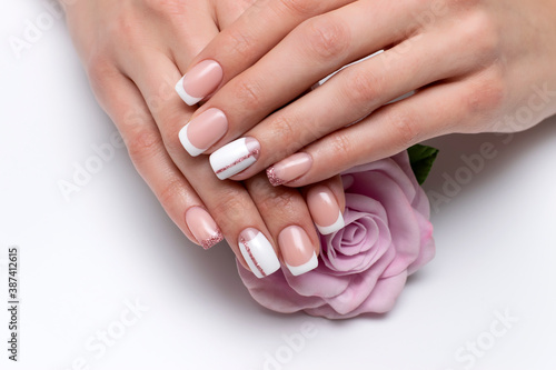 French bridal white manicure with pink glittery stripe and shiny little finger on long square nails close-up on a white background holding a pink rose.