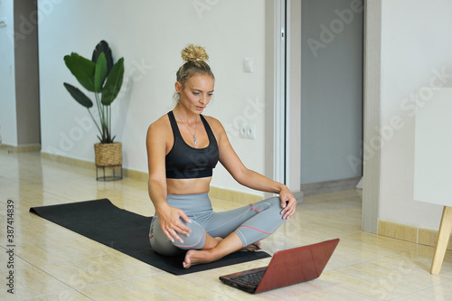 Mujer haciendo yoga en casa usando el portátil. Concepto confinamiento. photo