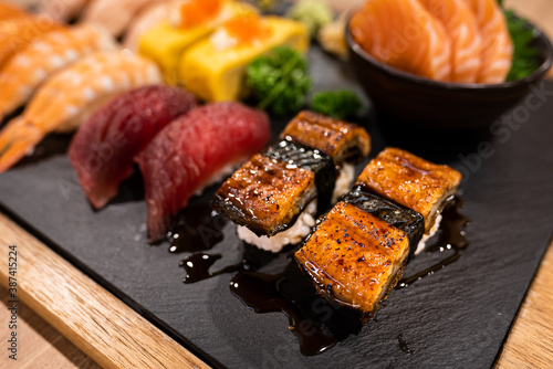 Piece of grilled Japanese eel (Unagi) with various types of sushi are served on the wooden table. Food object photo, selective focus at meat's part.
