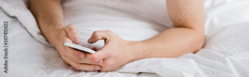 cropped view of man messaging on mobile phone in bed  banner