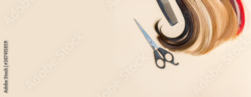 Hairdresser's scissors with comb and strand of hair on camel color background. Hairdresser service photo