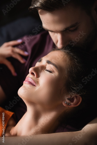young man calming depressed woman and kissing her head