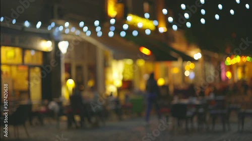 Slow motion shot of illuminated street with cafes and summer terraces. People walk along the pedestrian street of the old city and choose a place for dinner. Cozy restaurants for a romantic evening