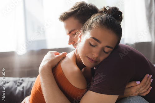 young, tender couple hugging with closed eyes while sitting at home photo