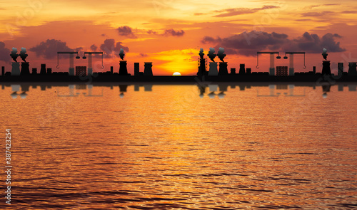 silhouette of large industrial  On the sea or river,Causing air pollution and  Water pollution.On the sunset background.Environmental conservation concept. © Mohwet