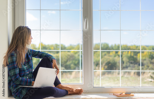 young relaxed woman looking out the window while using her laptop