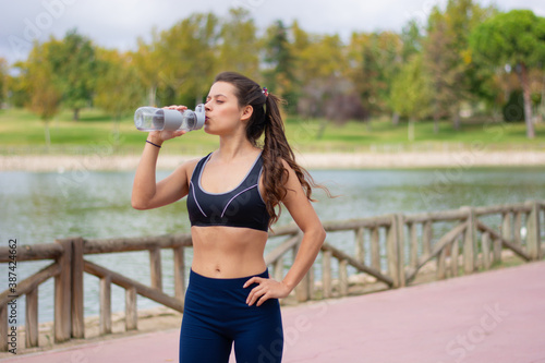 Instructor de fitness mujer delgada hermosa caucásica agua potable durante los ejercicios de entrenamiento al aire libre. mujer en ropa deportiva