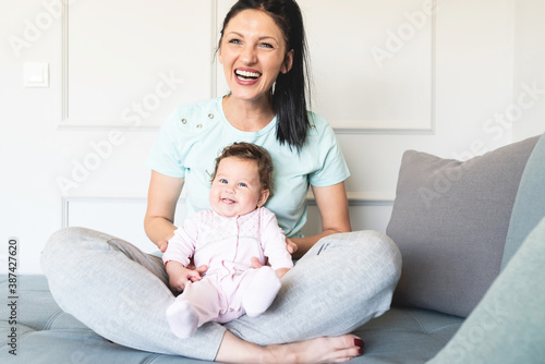 Happy mother sitting with cute baby daughter on sofa at home