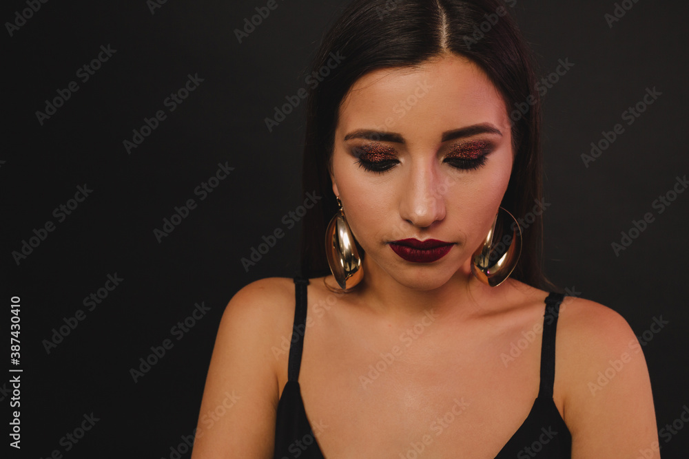 concentrated serious girl with dark lipstick and twinkling eyes with golden earrings posing over black background concentrated serious girl with dark lipstick and twinkling eyes with golden earrings posing over black background