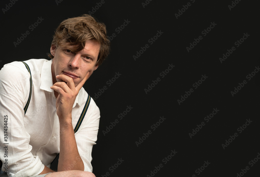 Thoughtful man in white shirt looks at camera against black background. Empty space for text.