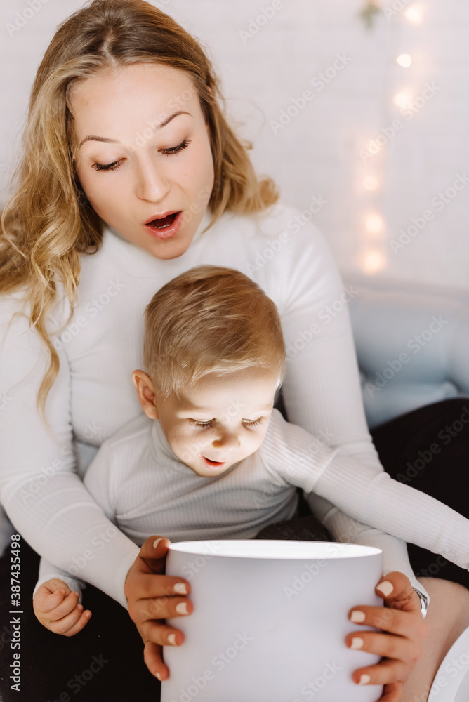 Little toddler boy with mom excitingly looking inside of glowing Christmas gift box. Little toddler boy with mom excitingly looking inside of glowing Christmas gift box.