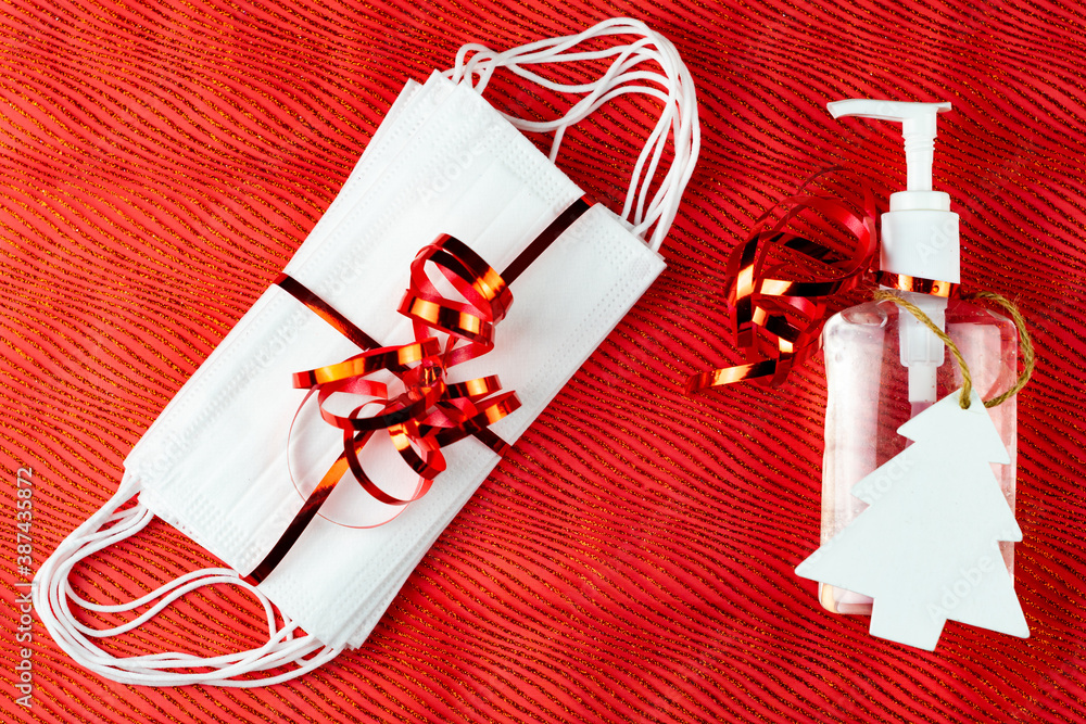 Bottle of hand gel sanitizer with Christmas decoration and ribbon as a gift. Concept of spending Christmas during coronavirus pandemic lock down and quarantine. Red background top view.