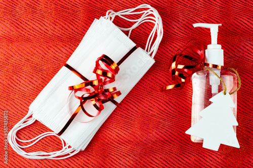 Obraz na płótnie Bottle of hand gel sanitizer with Christmas decoration and ribbon as a gift. Concept of spending Christmas during coronavirus pandemic lock down and quarantine. Red background top view. w salonie