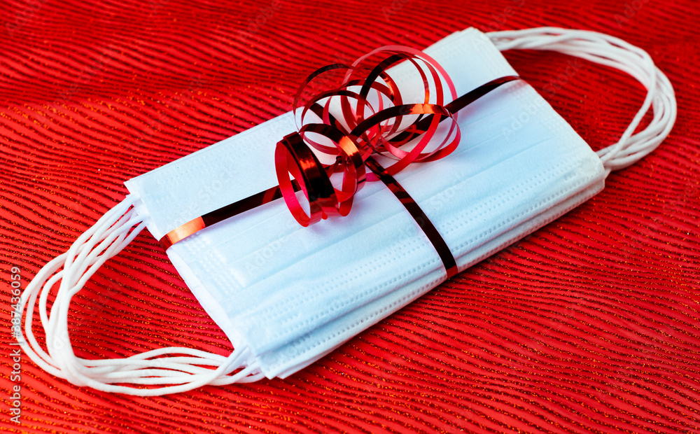 Protective face masks packed with ribbon as a Christmas gift on red background. Concept of coronavirus pandemic christmas time during the lockdown and quarantine.