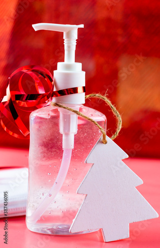 Obraz na płótnie Bottle of hand gel sanitizer with Christmas decoration and ribbon as a gift. Concept of spending Christmas during coronavirus pandemic lock down and quarantine. Red glittery background. w salonie