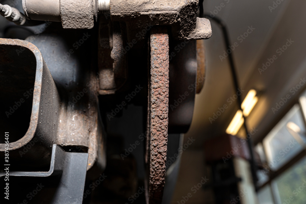Old and damaged rear brake discs with caliper and brake pads in the car, on a car lift in a workshop. Old and damaged rear brake discs with caliper and brake pads in the car, on a car lift in a workshop.
