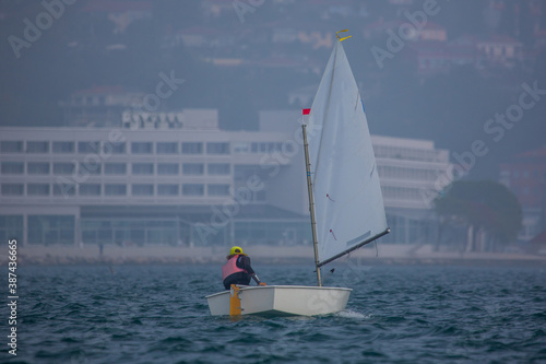 Back view of a sailor in a sailboat on a competition in Optimist class on open waters on the sea during sunny weather.