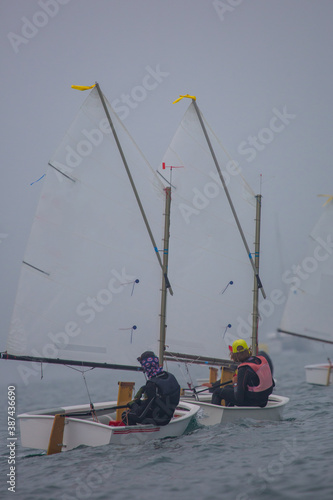 Back view of a sailor in a sailboat on a competition in Optimist class on open waters on the sea during cloudy weather.