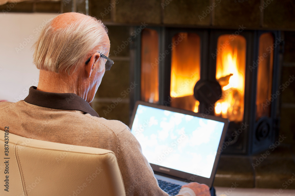 Senior man sitting by a fireplace and working with laptop Senior man sitting by a fireplace and working with laptop