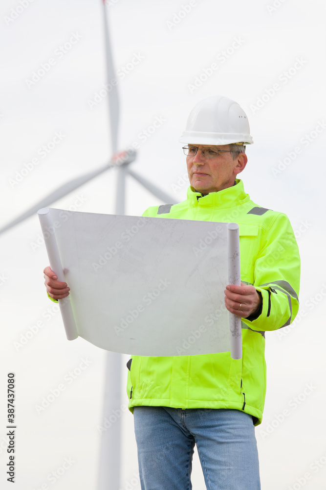 Mature engineer standing in front of a wind turbine with blueprint in his hand Mature engineer standing in front of a wind turbine with blueprint in his hand