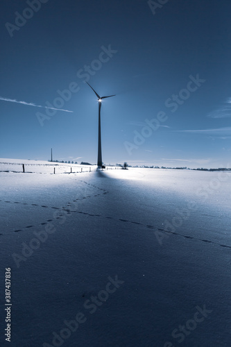 Wind Turbine in winter on a field with sunflare and shadows of the blades