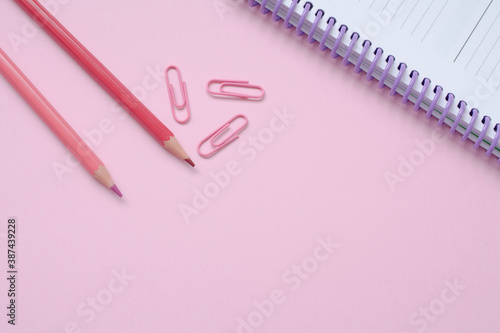Pink pencils, paper clips and a notebook over a pink background.