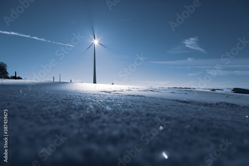 Wind Turbine in winter on a field with sunflare and shadows of the blades