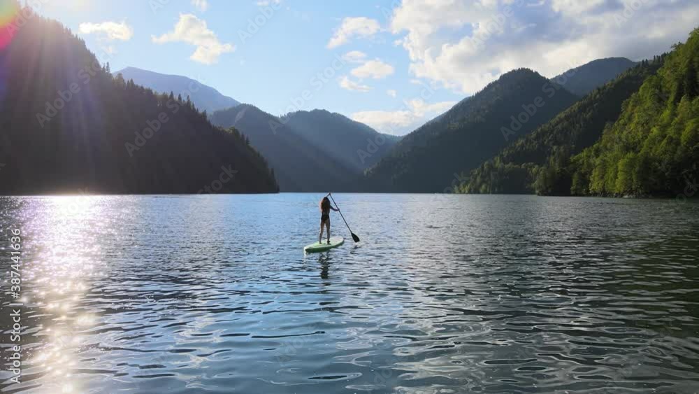 Concept of active tourism and travel. Aerial drone view of woman silhouette paddle on sup surfing board at mountain lake during sunset. Sporty girl doing water sport during summer holidays. Concept of active tourism and travel. Aerial drone view of woman silhouette paddle on sup surfing board at mountain lake during sunset. Sporty girl doing water sport during summer holidays.