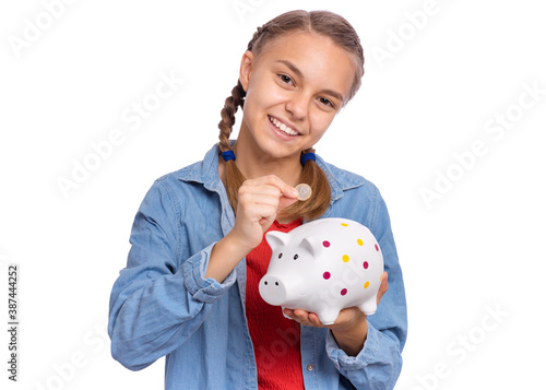 Beautiful teenage girl holds a piggy bank and a coin in her hands, isolated on white background photo