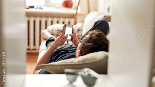 Принти на полотні Teenage guy using his mobile phone while lying on the couch at home