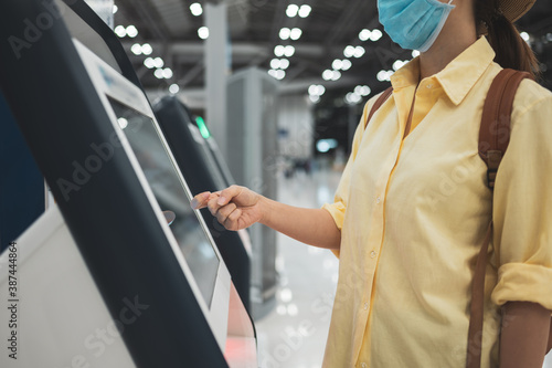 Asian woman wearing face mask self checking-in printing a boarding pass at the airport while coronavirus pandemic concept of Safety travel under COVID-19 speading
