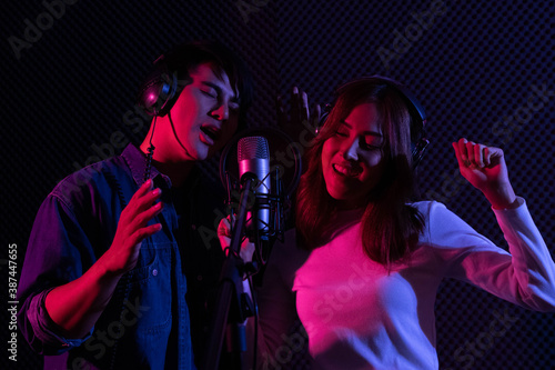 Billede på lærred Young Asian man and woman singing to condenser microphone in studio