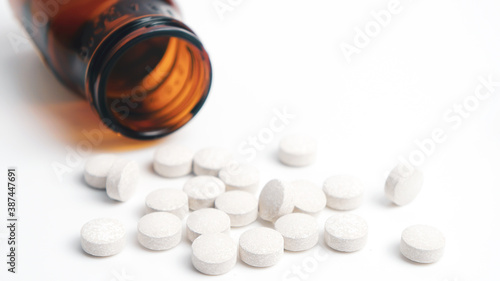 Round medical pill scattered in front of the bottle. 