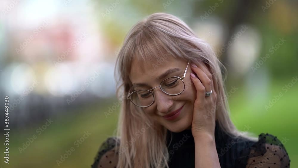 Close-up portrait of a young smiling blonde woman with glasses posing straightening her hair while walking around the city in a Park on an autumn day. Close-up portrait of a young smiling blonde woman with glasses posing straightening her hair while walking around the city in a Park on an autumn day.