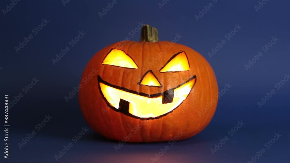 Halloween pumpkin or jack-o-lantern with glowing eyes on a blue background. jack-o-lantern for a Halloween party stands on a table against a dark background. Preparing to celebrate Halloween. Halloween pumpkin or jack-o-lantern with glowing eyes on a blue background. jack-o-lantern for a Halloween party stands on a table against a dark background. Preparing to celebrate Halloween.