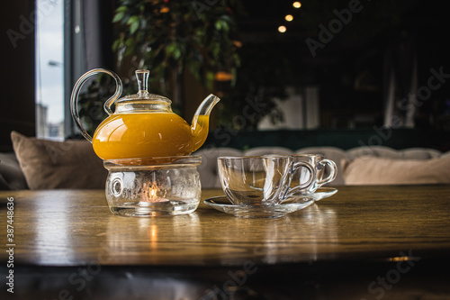 Herbal sea buckthorn tea in a transparent teapot and in a transparent glass with double heating bottom in restaurant. Concept of warmth and comfort. Mango and passion fruit tea