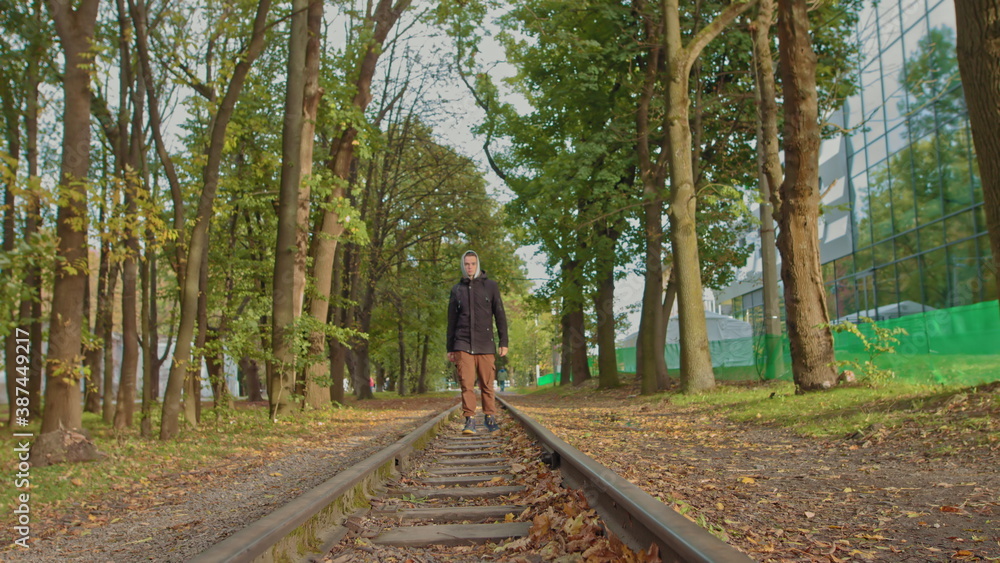 A young guy confidently moves to the camera in the park on the track, a stylishly dressed teenager.