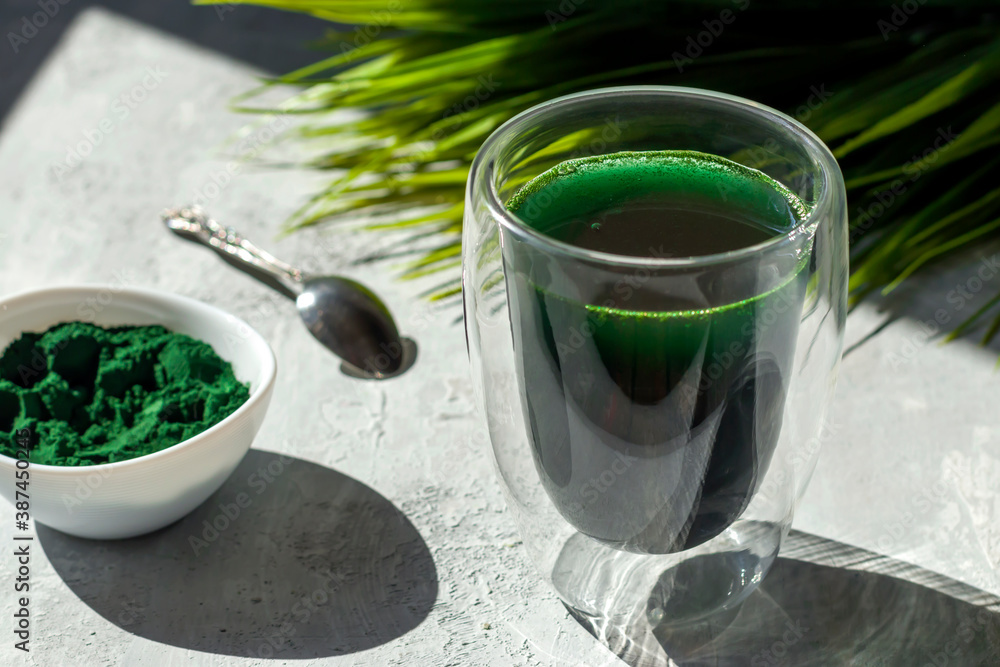 Spirulina drink with and spirulina algae powder on white plate. Superfood detox drink. Natural antioxidant. Anti-aging effect. Green diet. Hard shadows. Spirulina drink with and spirulina algae powder on white plate. Superfood detox drink. Natural antioxidant. Anti-aging effect. Green diet. Hard shadows.