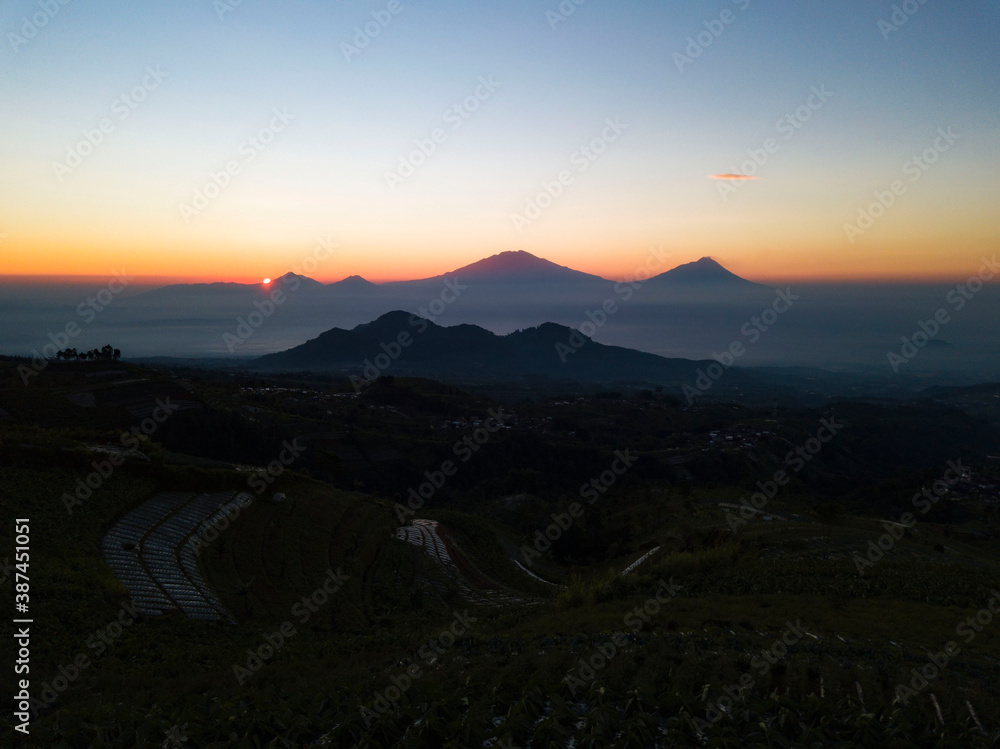 Vagetable plantation with sunrise sky on the background. Seen mountains on the horizon and cloudy sky. Slope of mout sumbing, Silancur Highland, Magelang, Central Java, Indonesia