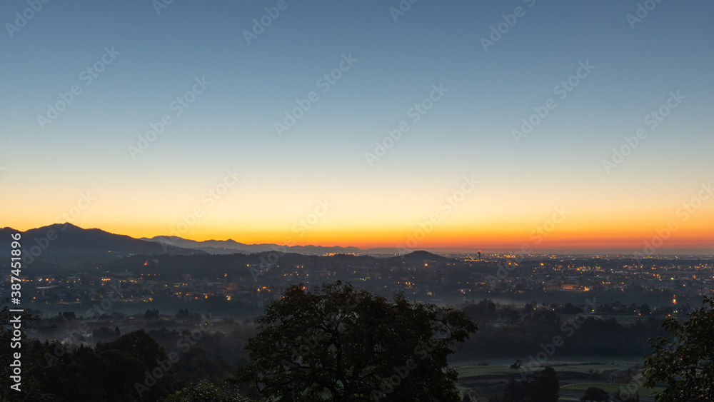 A clear sky lights up during the sunrise over the plain with the last city lights